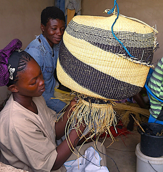 Kvinde færdiggør en håndvævet kurv i Ghana